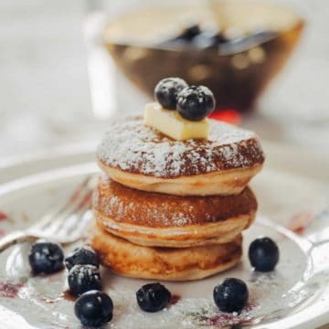 a stack of pikelets on a white plate with blueberries.