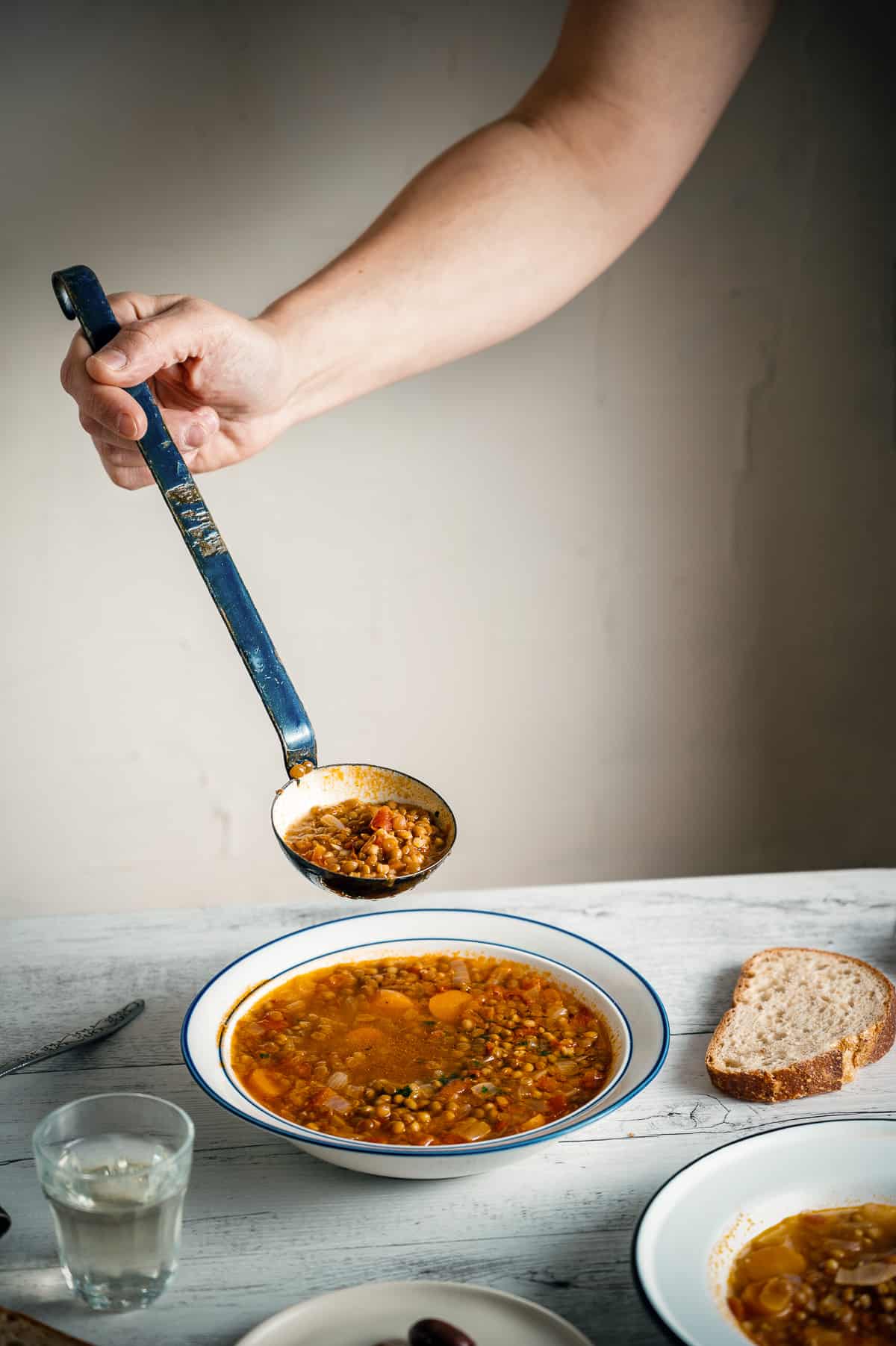 a hand using a ladle to serve Greek lentil soup in a bowl