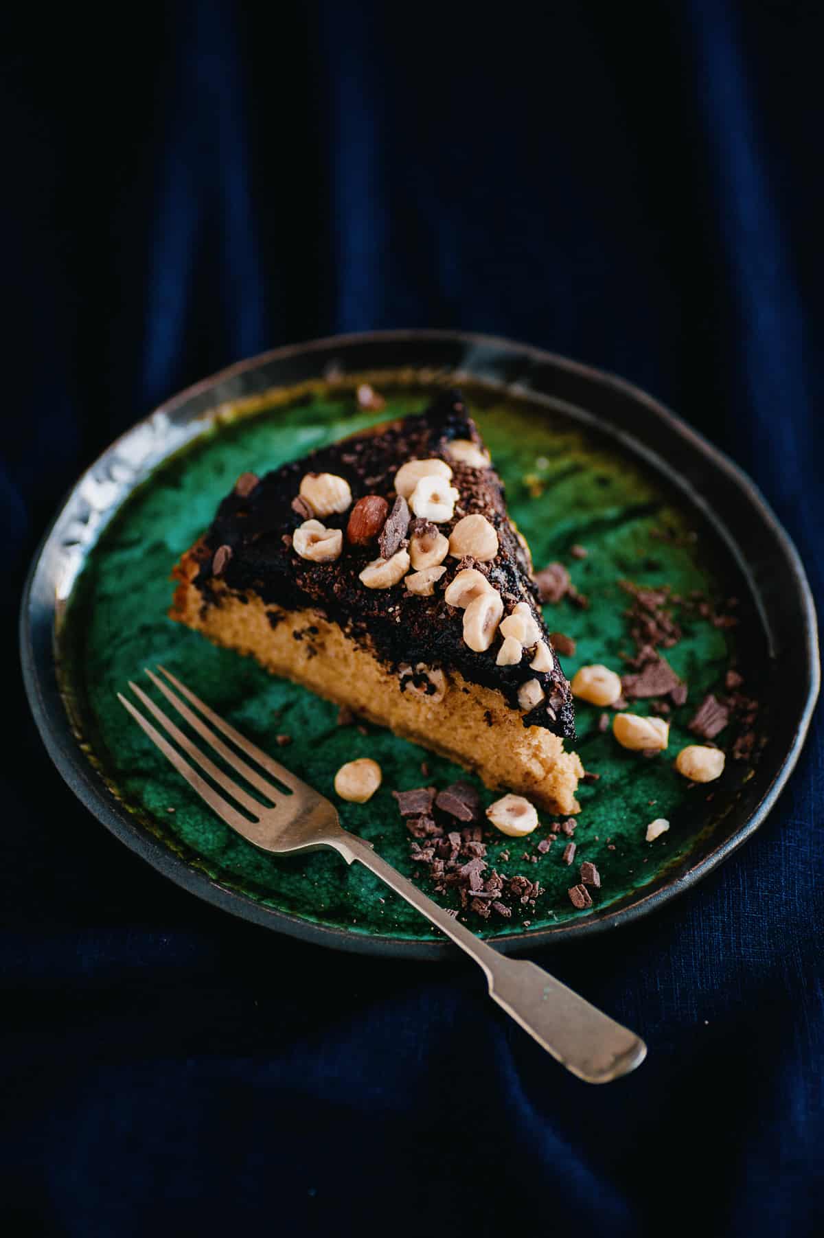 a slice of cake on a plate. the cake is covered in a chocolate spread and covered hazelnuts