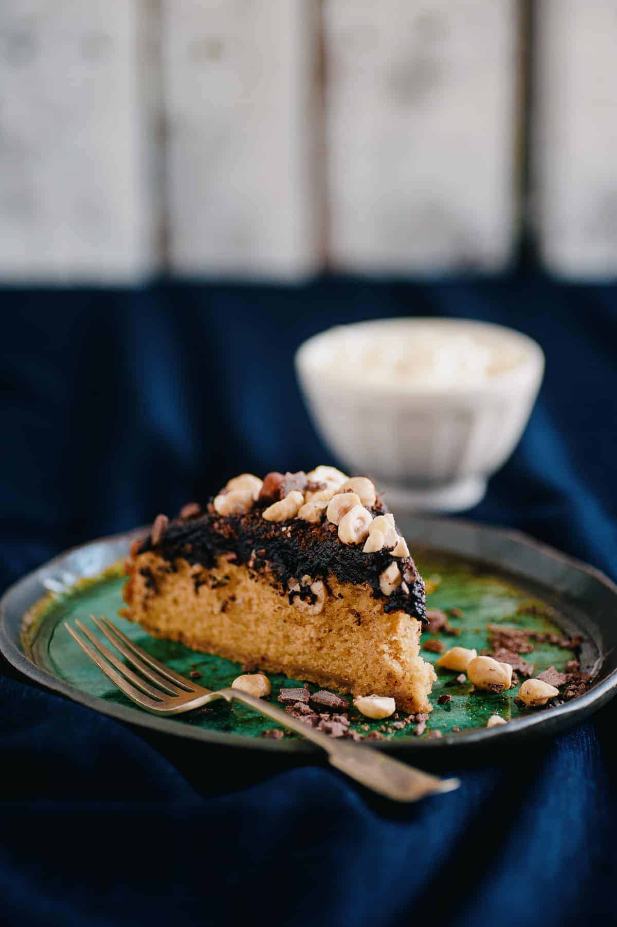 a slice of cake on a plate. the cake is covered in a chocolate spread and covered hazelnuts