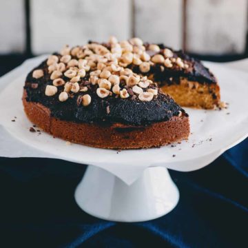 a cake on a cake stand topped with a chocolate spread and raw hazelnuts
