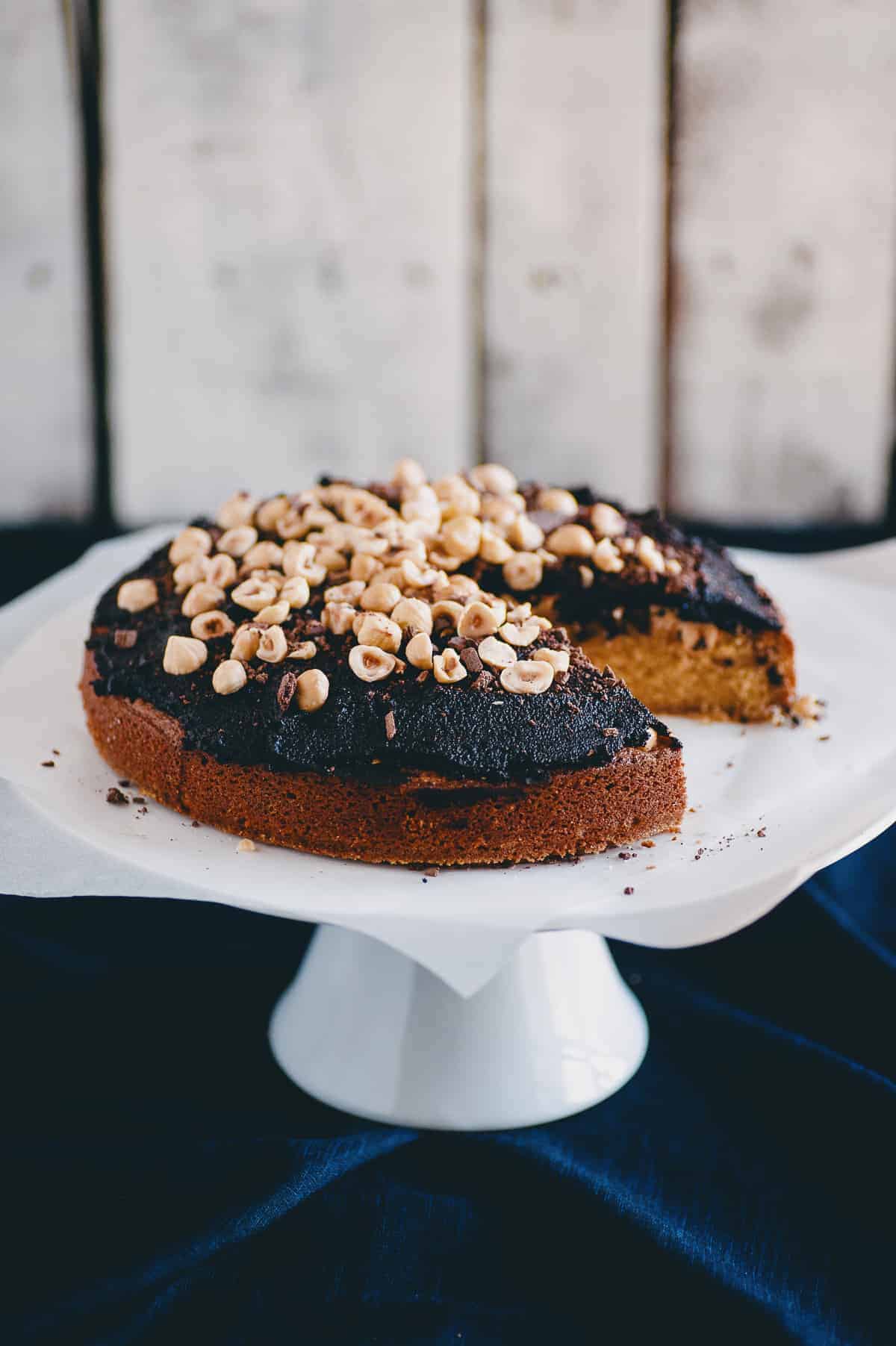 a cake on a cake stand topped with a chocolate spread and raw hazelnuts