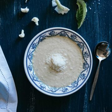 a bowl of cauliflower soup served in a bowl on top of a blue table