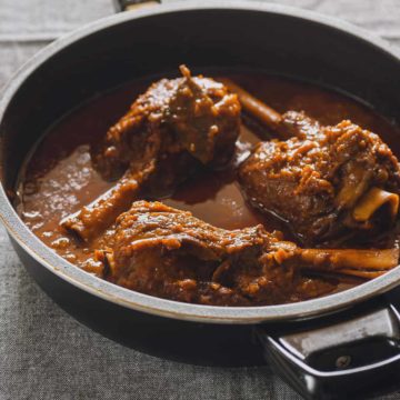 three braised lamb shanks in a black pan