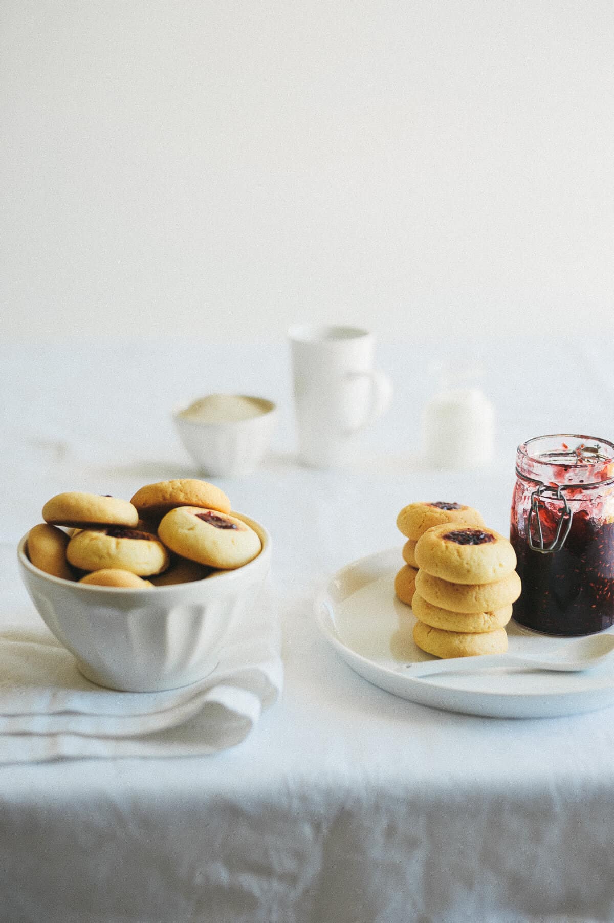 a white table that hands a bowl filled with biscuits and a plate with a jar of jam