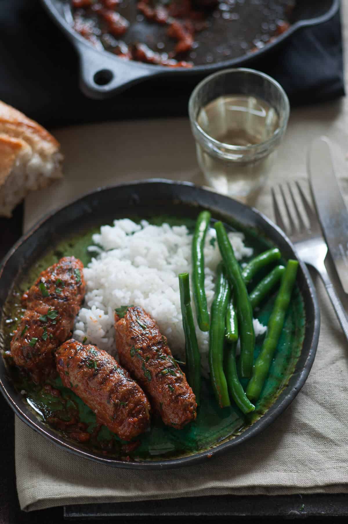 three oblong meatballs served on a plate with rice and green beans