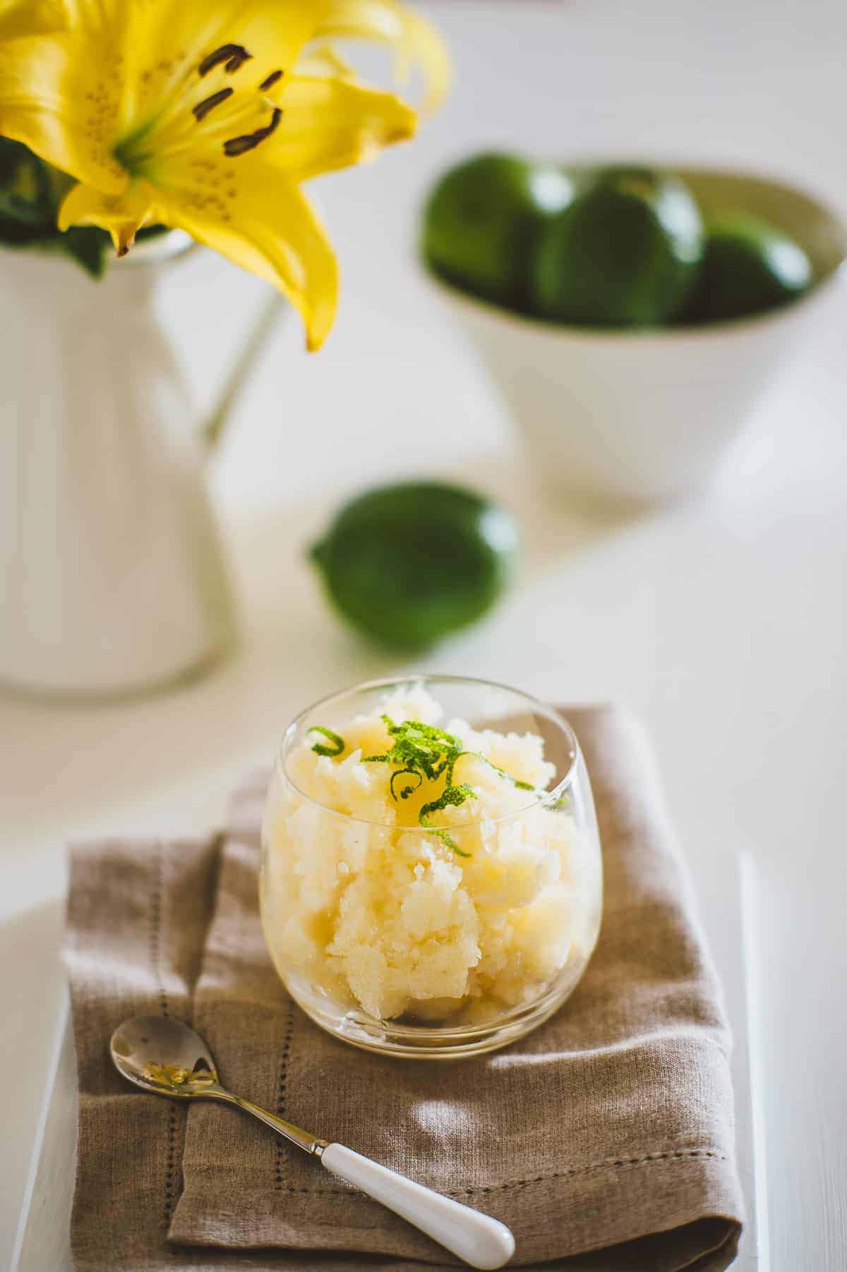 a glass filled with homemade pineapple granita on a cloth surrounded by limes and flowers