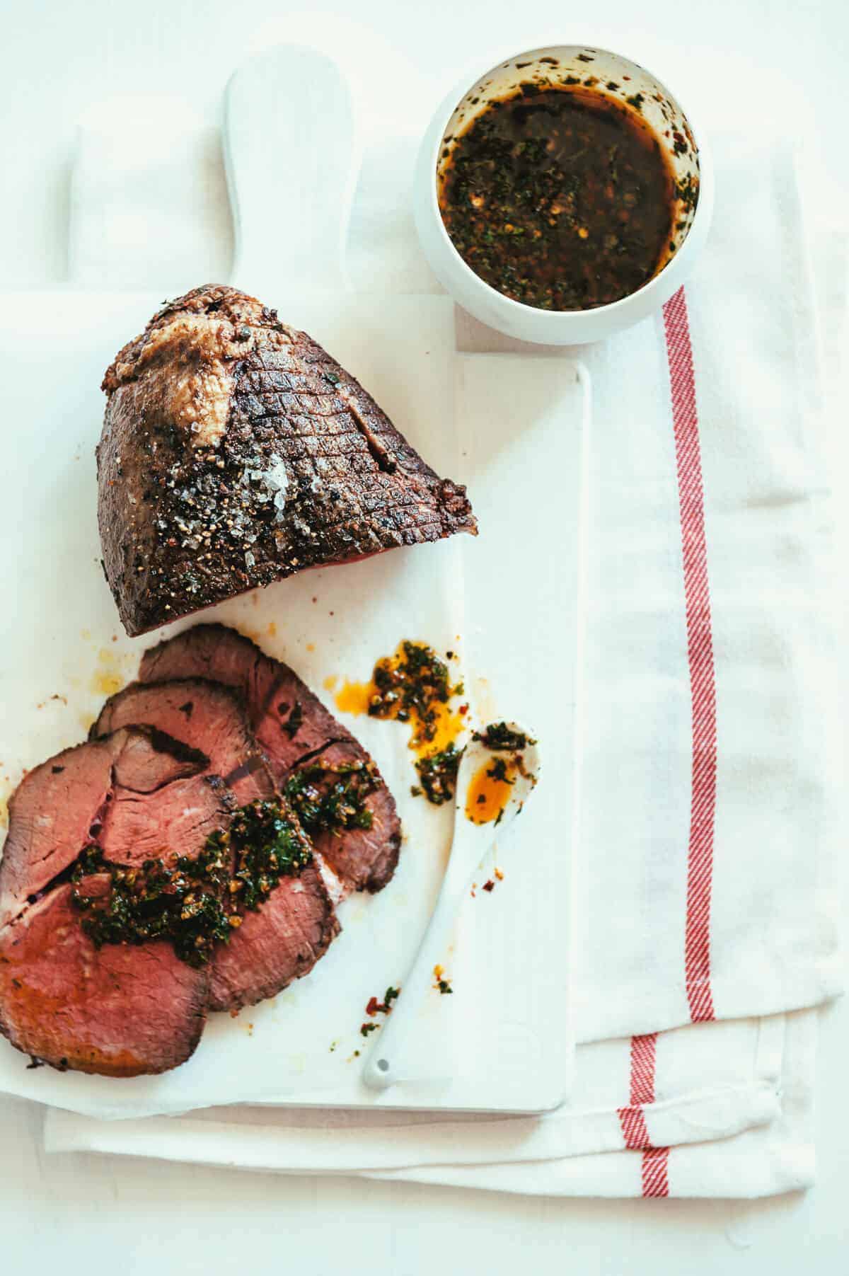 birds eye view of a sliced roast meat served with an oily herb sauce