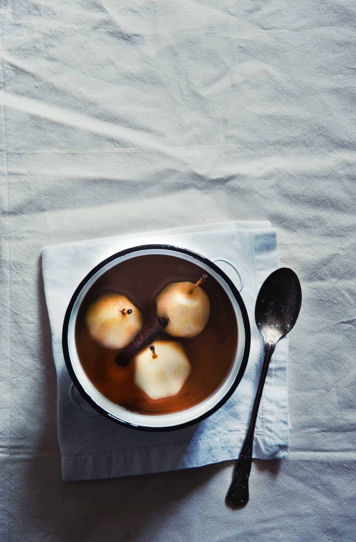 three poached pears in a white pot