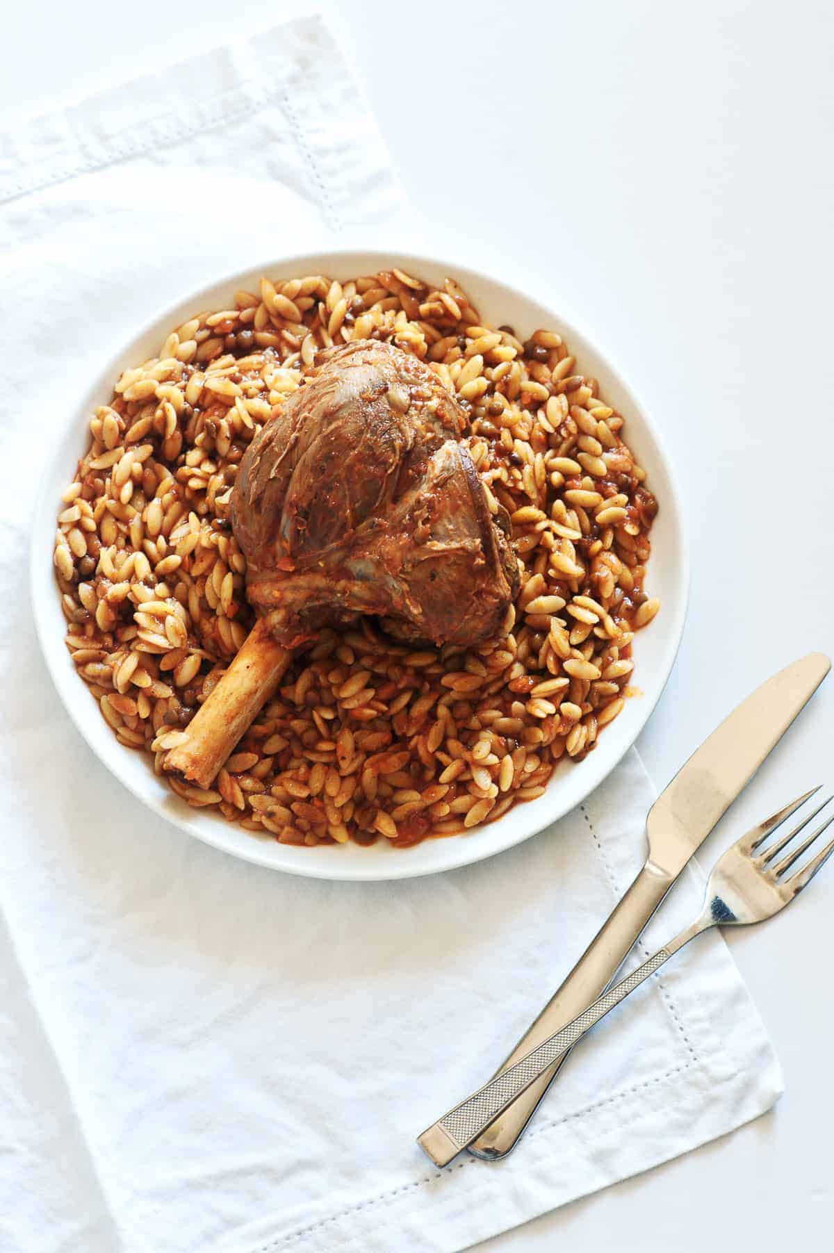 a birds eye view of a a braised lamb shank served with orzo pasta on a white plate