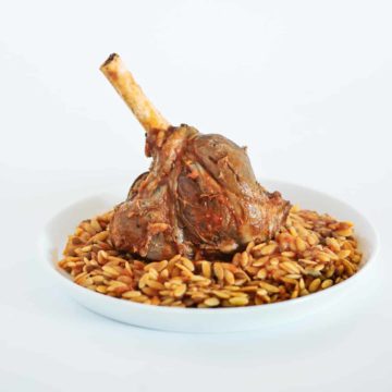 a braised lamb shank served with orzo pasta on a white plate