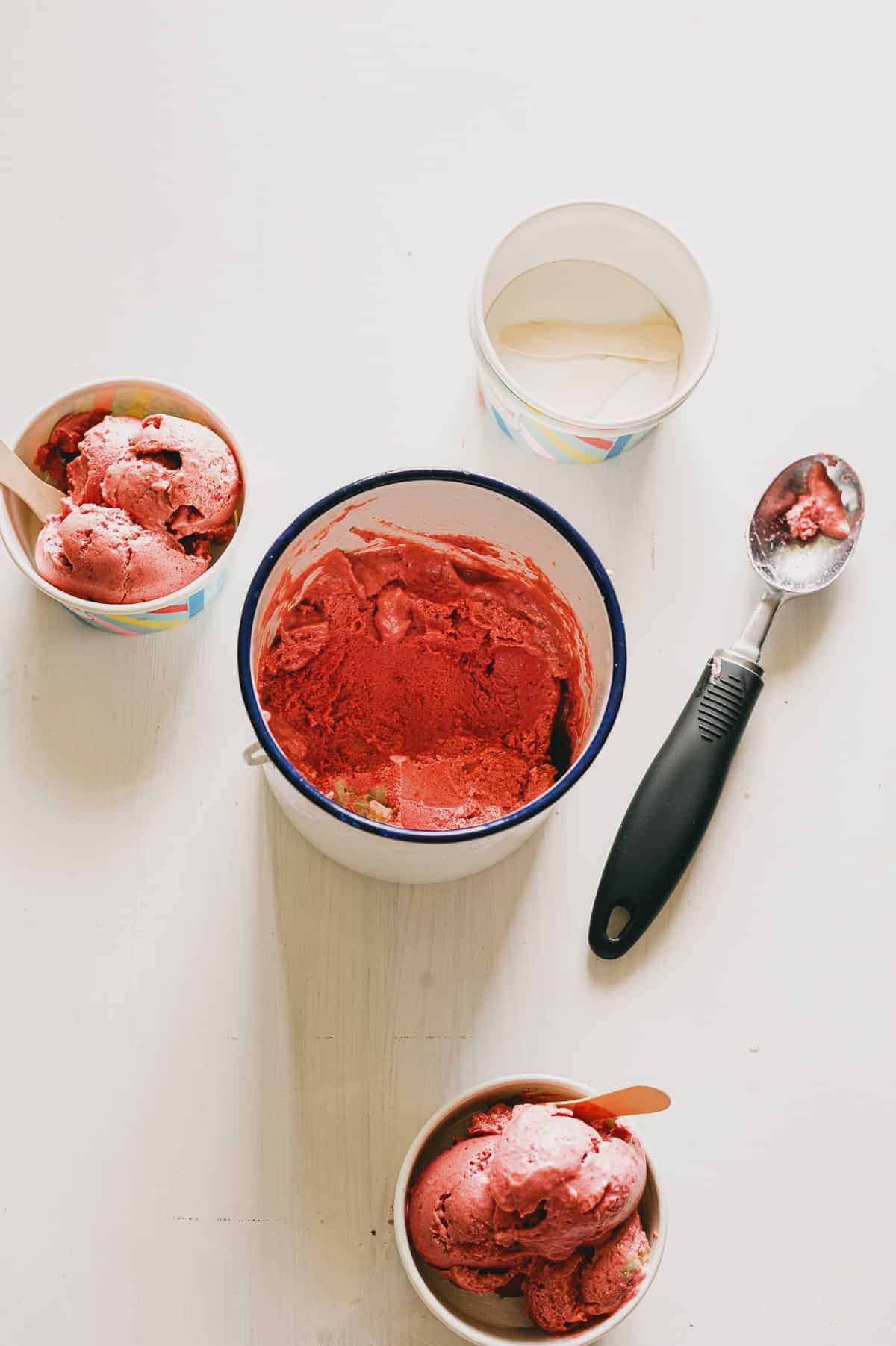 a tub of vegan raspberry ice cream  being scooped into two small containers on a white table