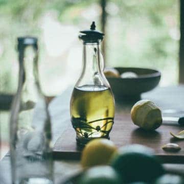 a bottle filled with olive oil on a table with peeled limes and lemons