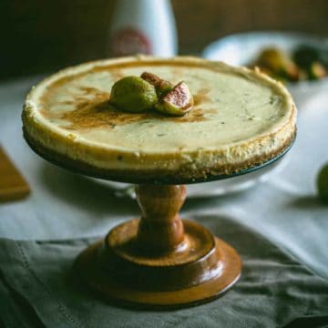 a cheesecake on a wooden cake stand topped with figs
