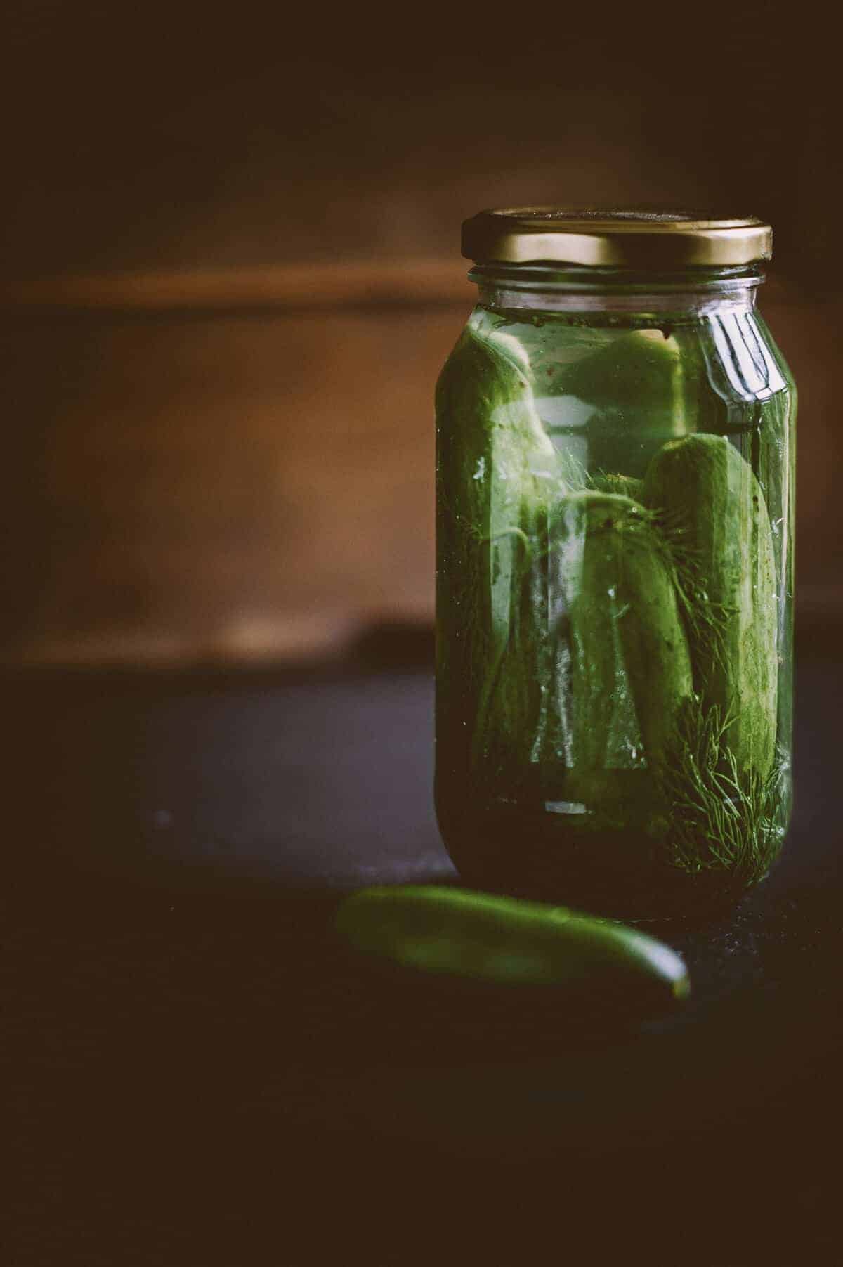 a glass jar full of pickles on a dark table with a wooden background