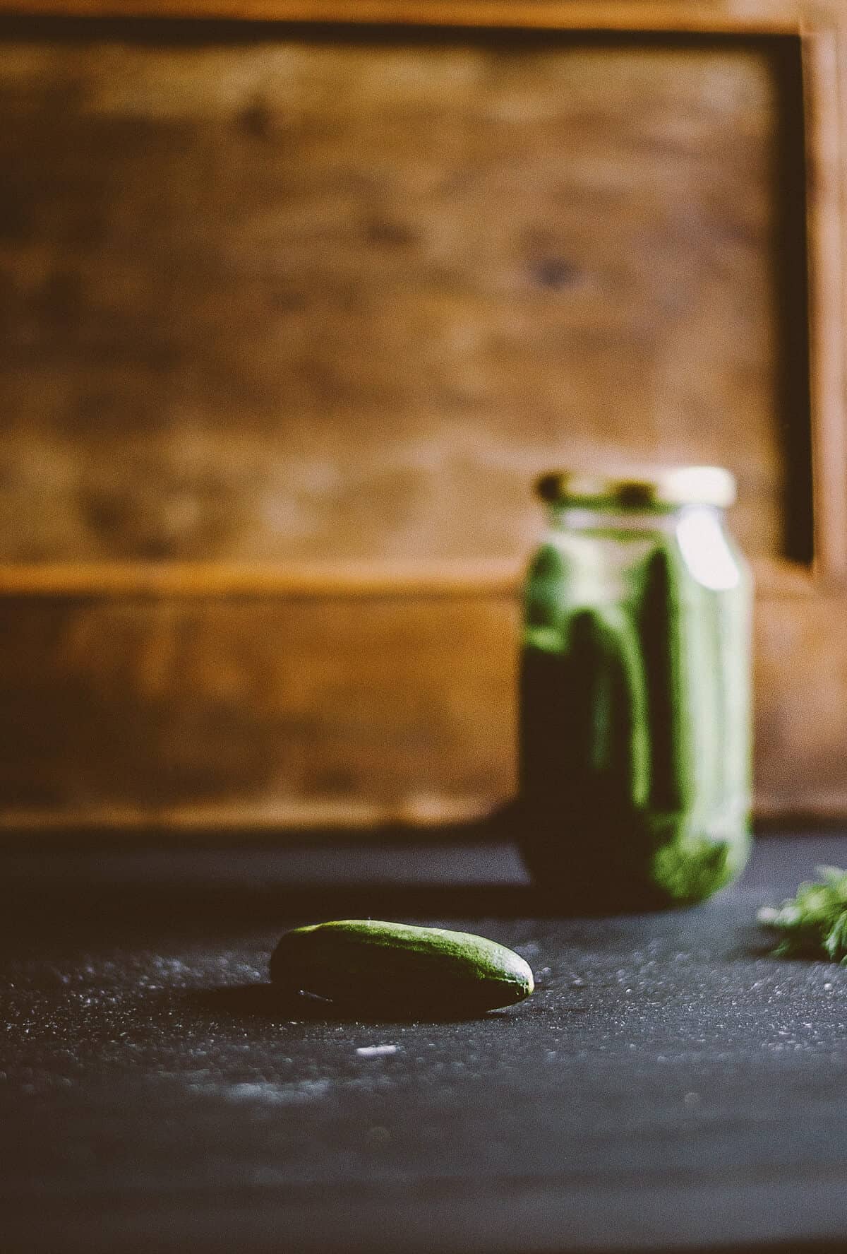 a glass jar full of pickles on a dark table with a wooden background