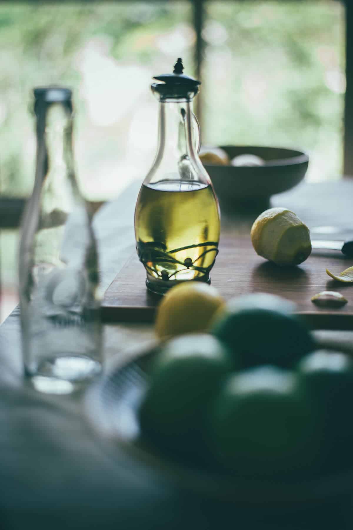 a bottle of olive oil with limes and lemons on a table