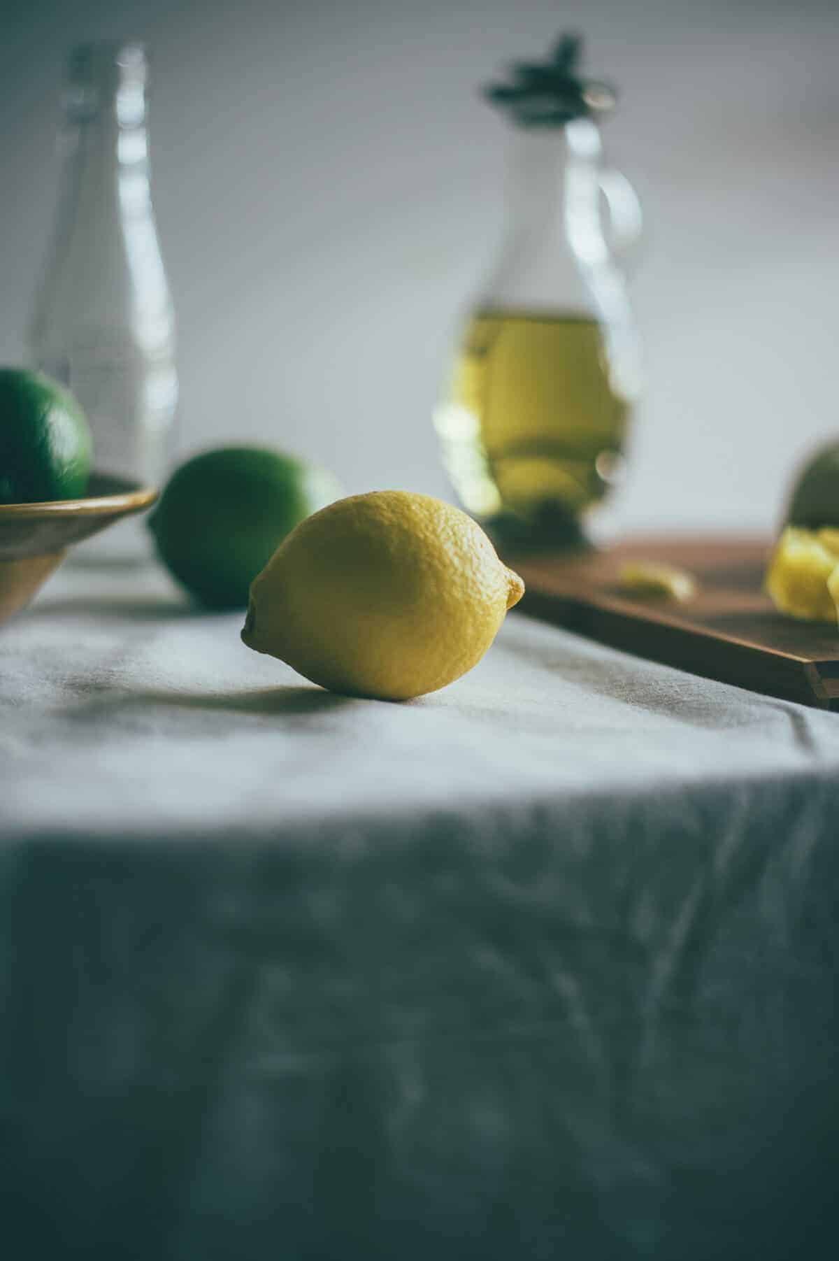 a whole lemon with limes on a table with a bottle of olive oil