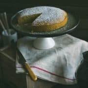 a cake on a cake stand sitting on top of a wooden box with a kitchen towel draped over it