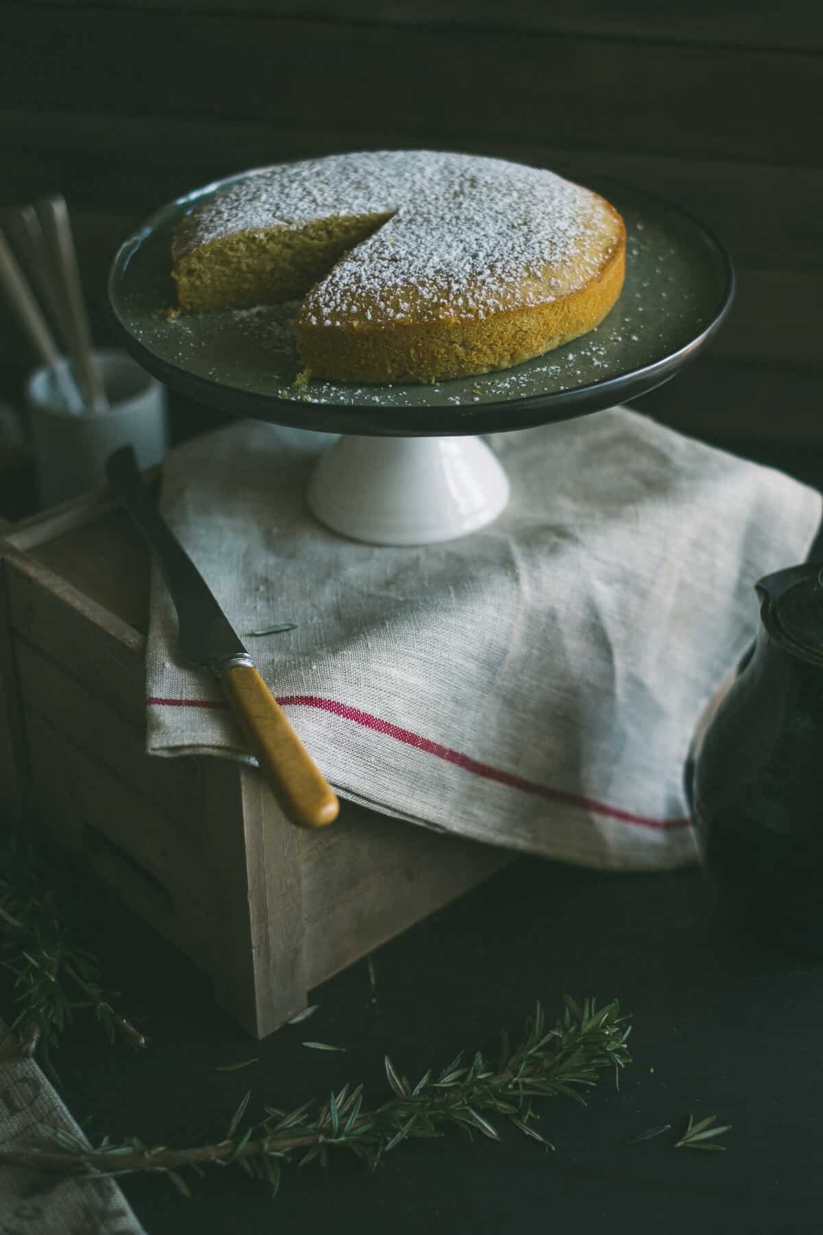 a cake on a cake stand sitting on top of a wooden box with a kitchen towel draped over it