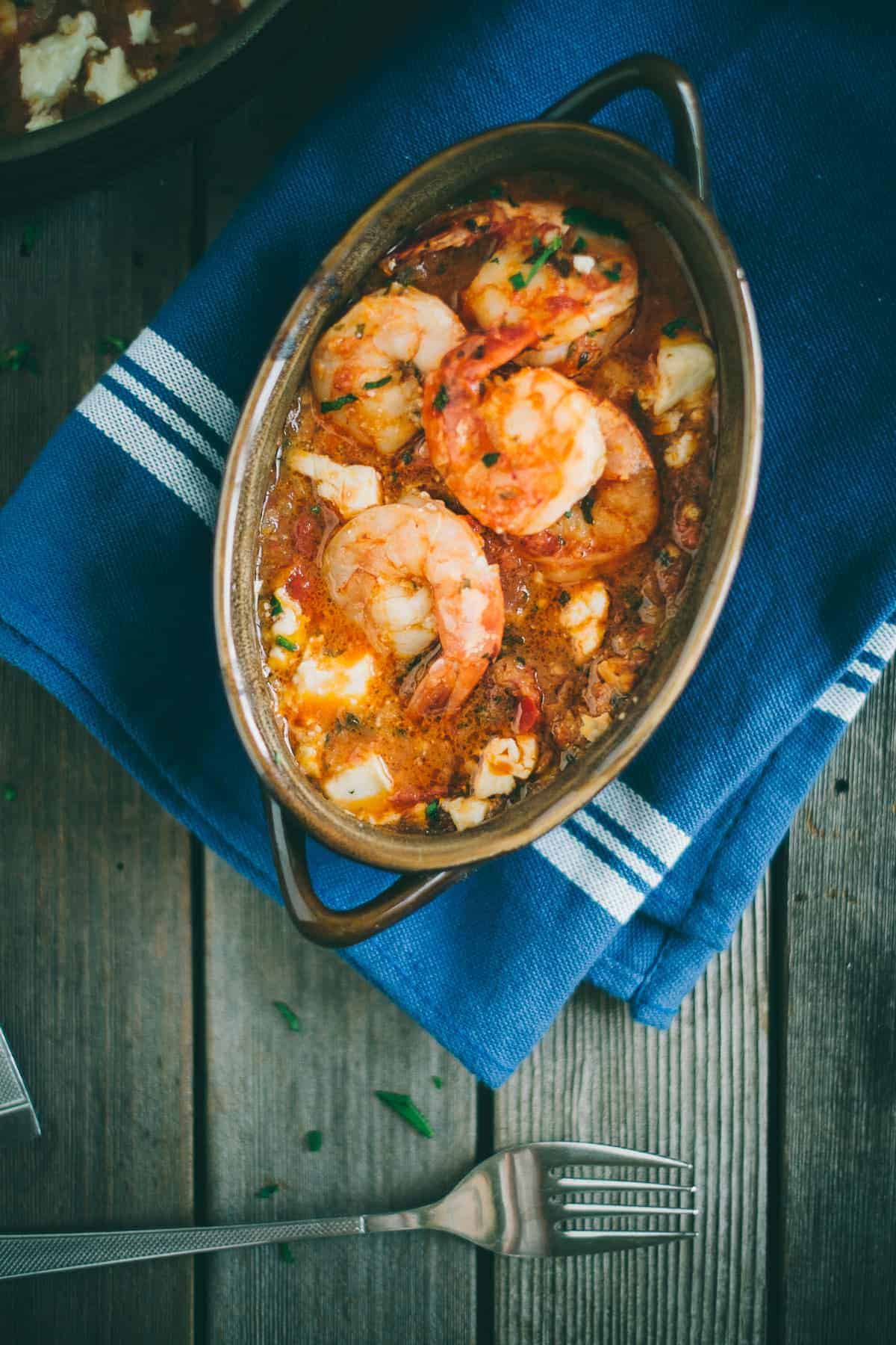 Prawn saganaki served in a claypot dish with ouzo on a wooden table