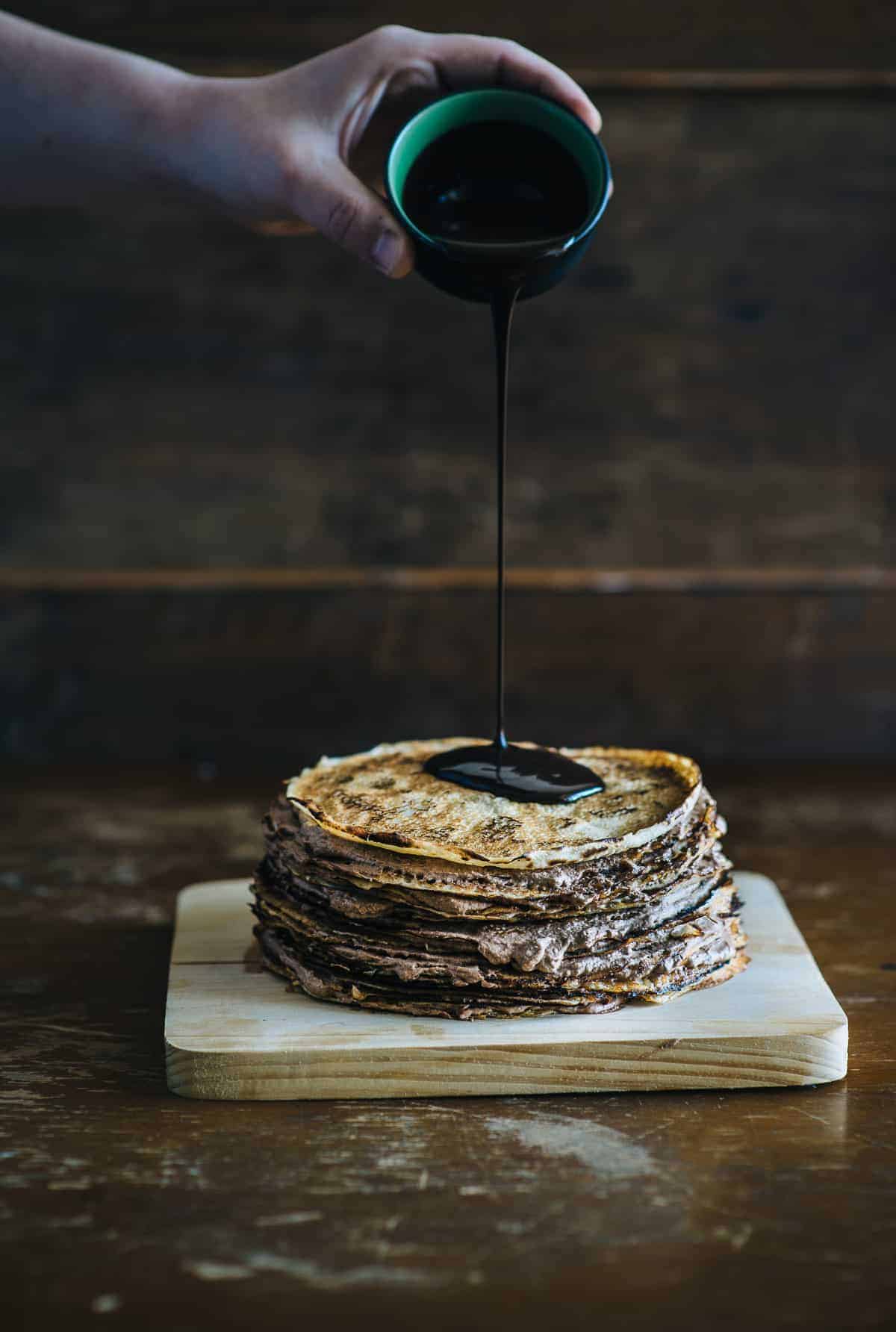 pouring chocolate over Nutella crepe cake