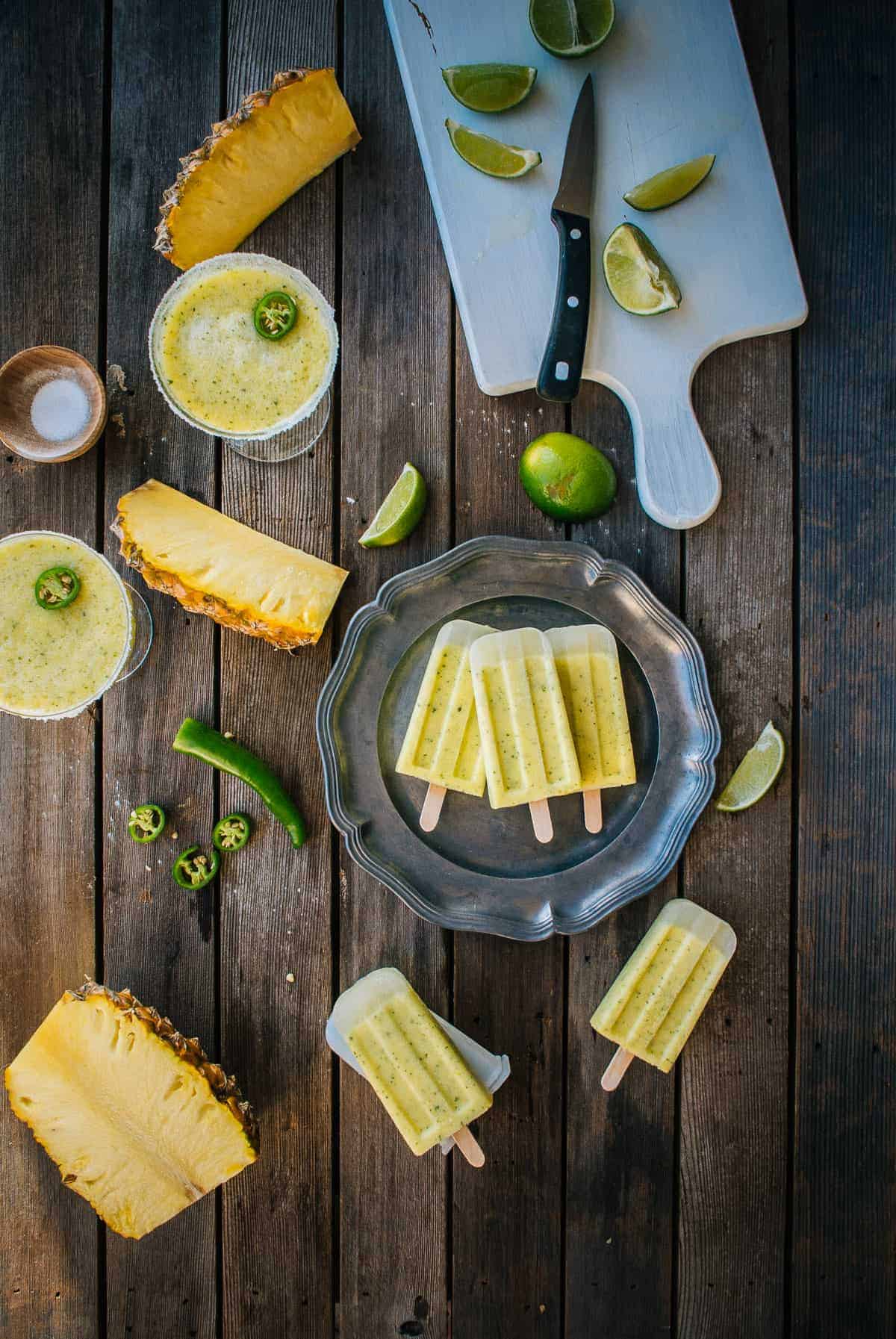 Homemade pineapple margarita ice pops served on a plate with fresh pineapple and limes