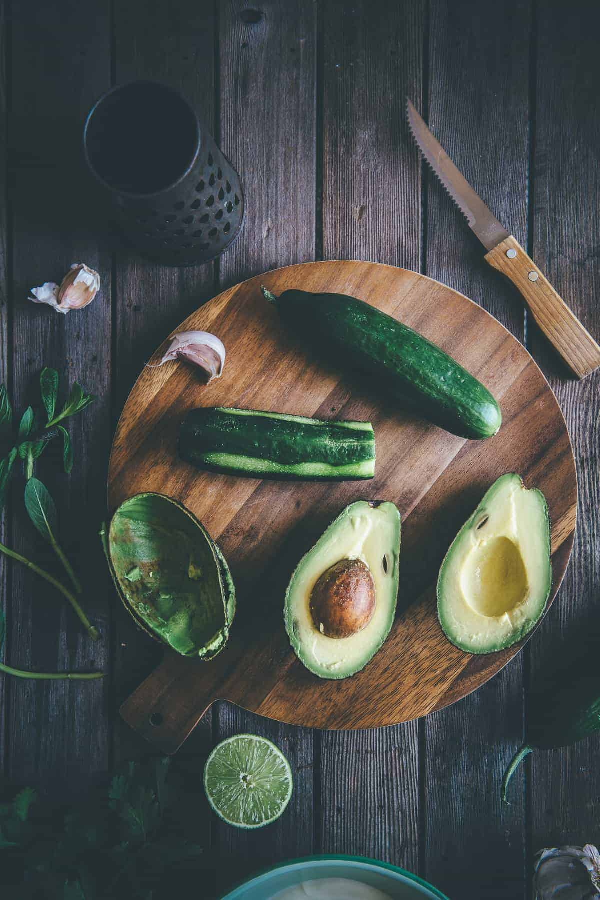 cucumbers and avocado laid out on a chopping being prepped to make avocado tzatziki