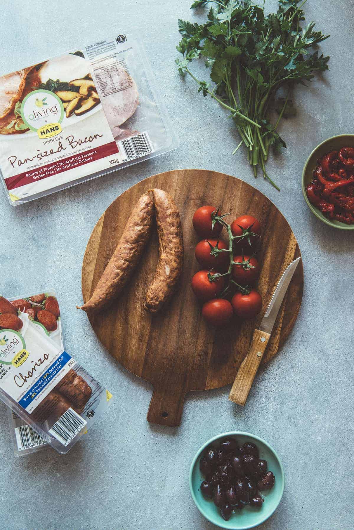 sausages and tomatoes on a chopping board with herbs 