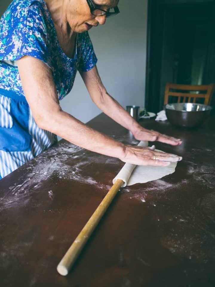 Greek mother rolling out homemade fillo dough on a table for spanakopita