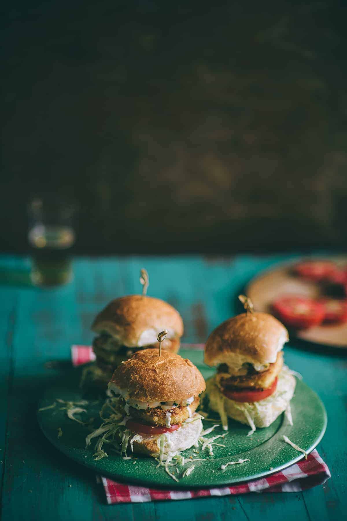 three burgers on a green plate on a rustic green table