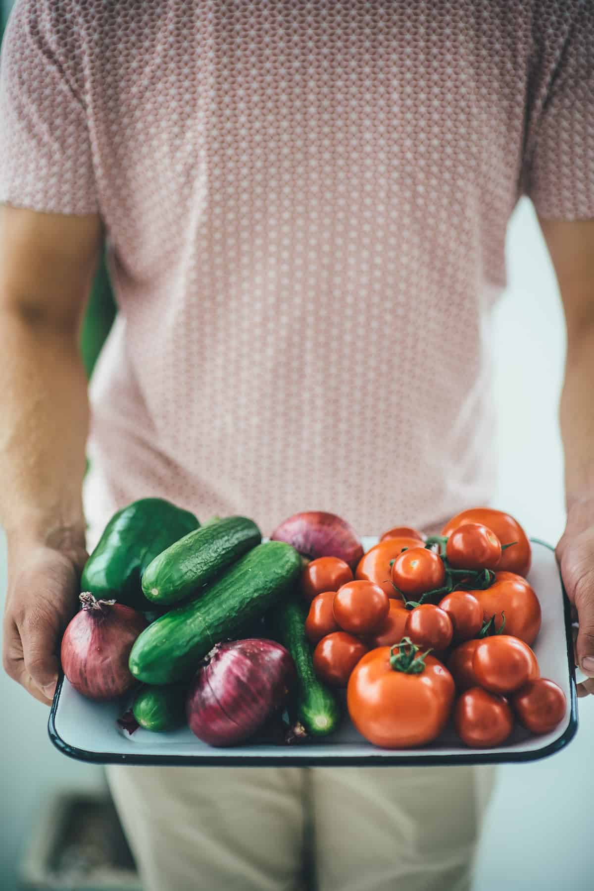 a man holding a tray filled with cucumbers tomatoes and onions