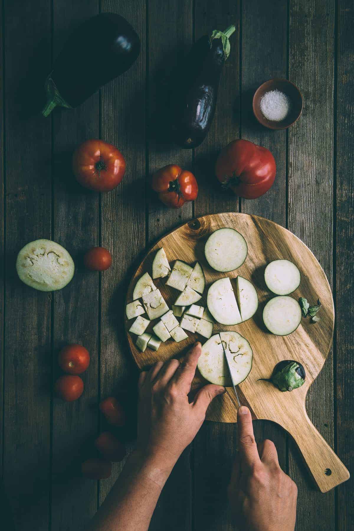 eggplants and tomatoes being cut on a chopping board