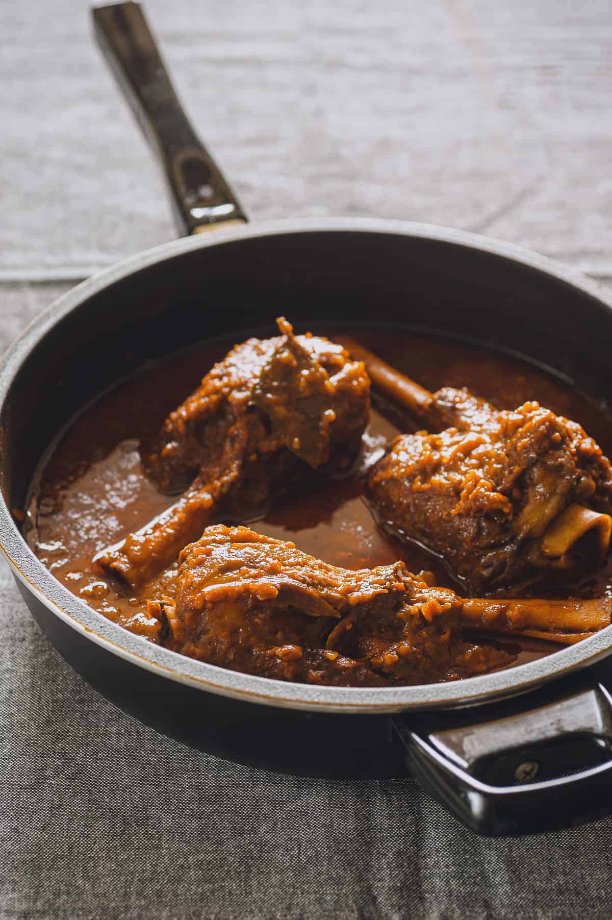 a pan filled with three cooked lamb shanks covered in a red sauce