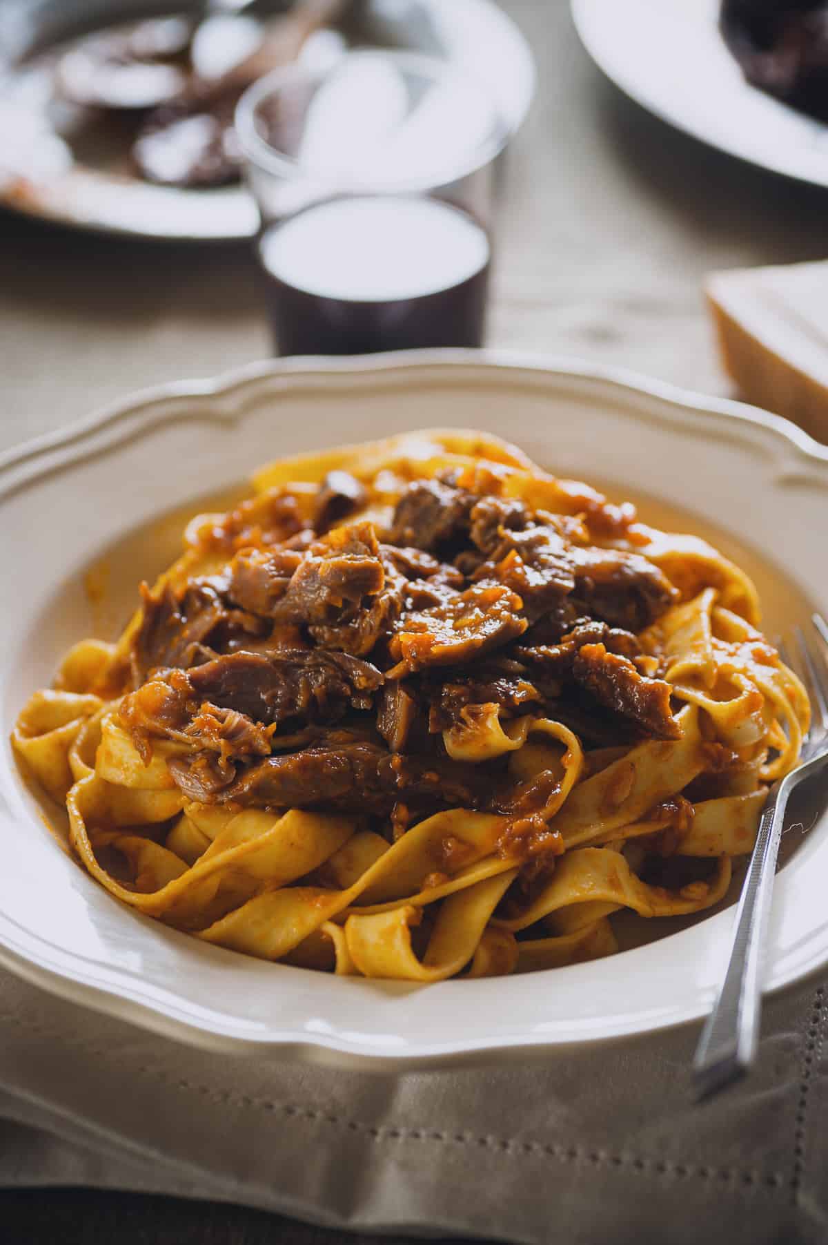 a white bowl filled with cooked noodles topped with a meat sauce