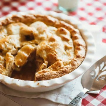 a baking dish with an apple pie on a table with a glass of milk