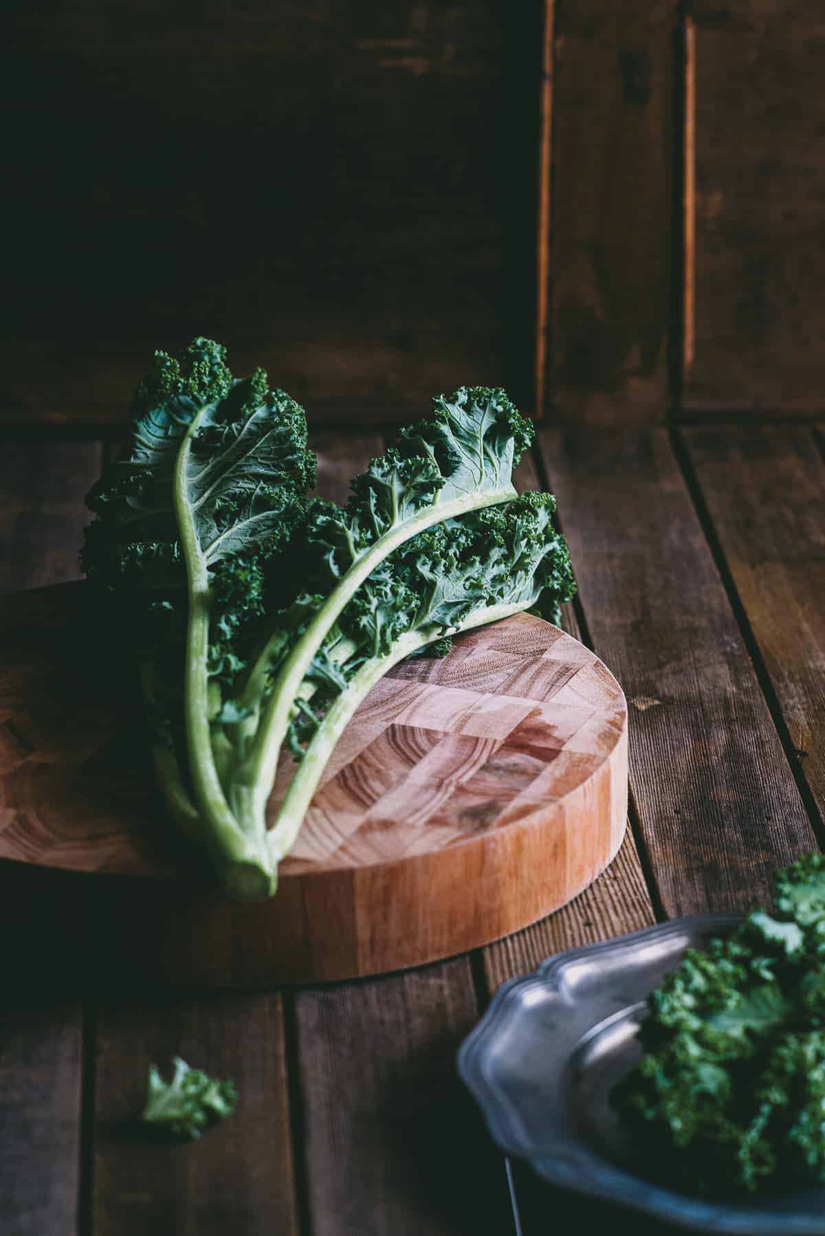 a bunch of kale on a round wooden chopping board 