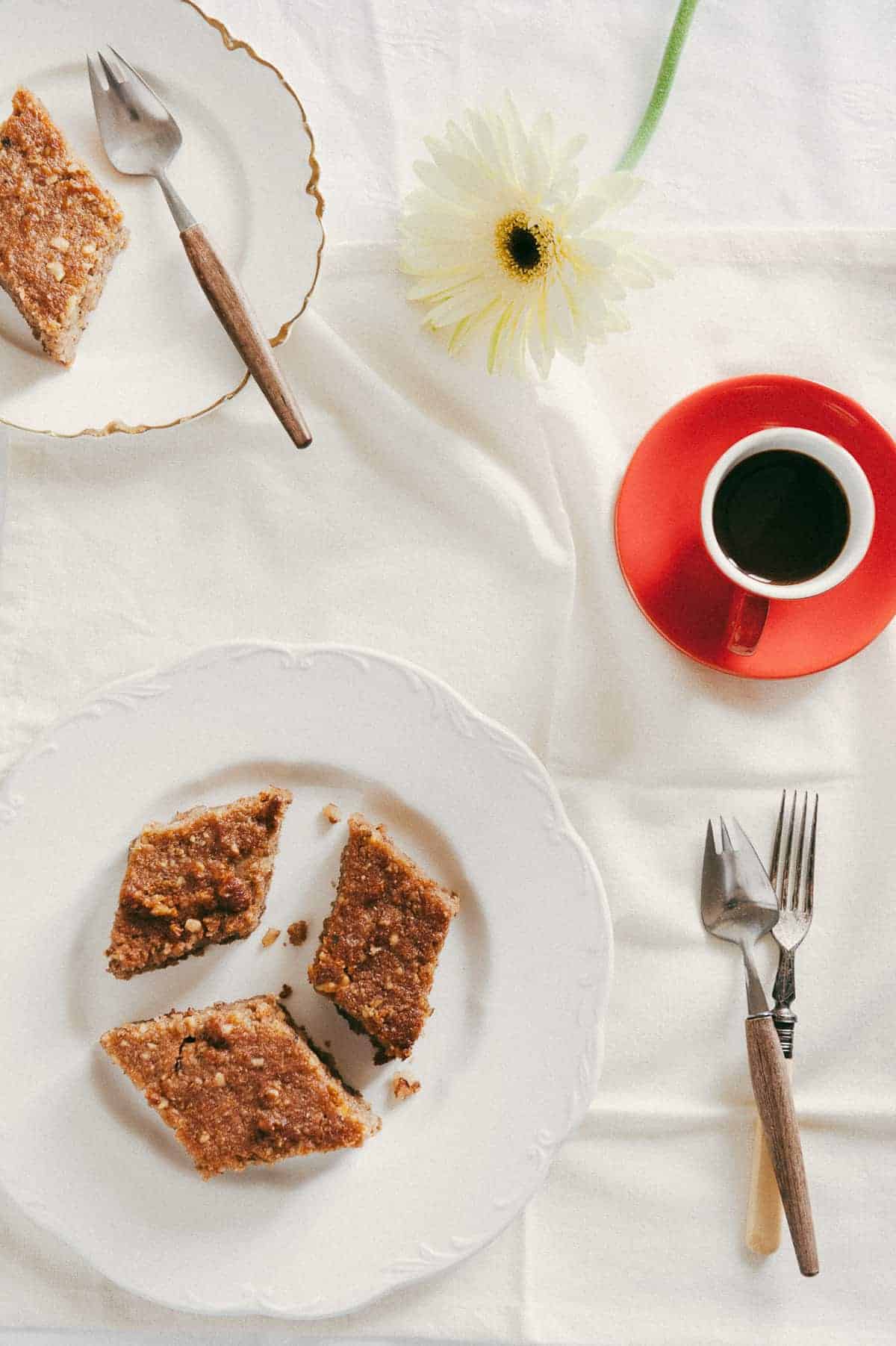 top down view of three slices of Greek walnut cake served on a white plate with a coffee and flowers