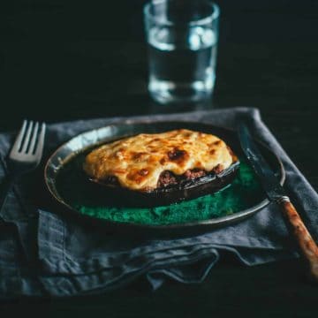 a green plate with a cooked eggplant which has been stuffed with a meat sauce and topped with a béchamel sauce