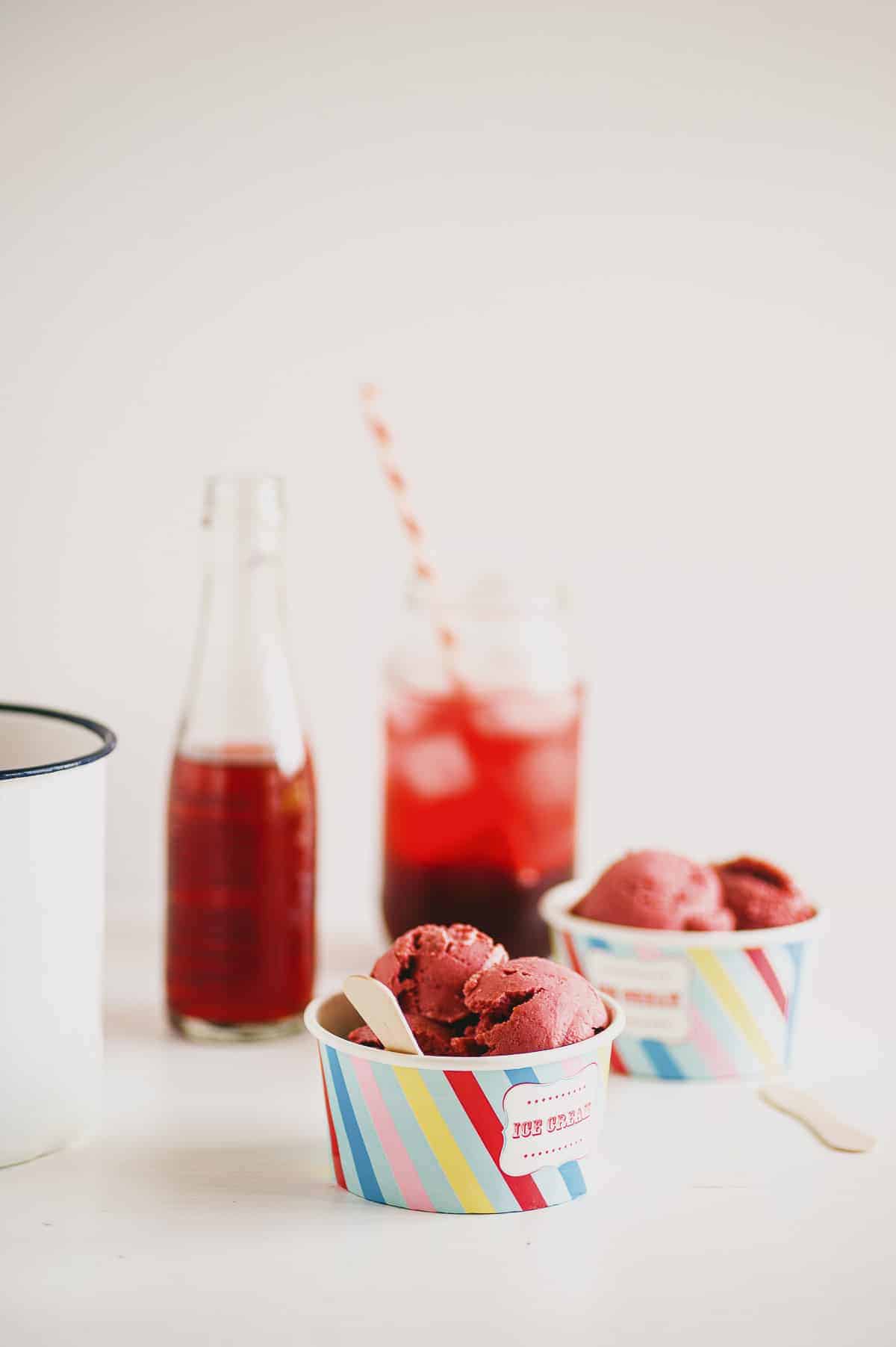 two small tubs of raspberry ice cream with two red drinks in the background