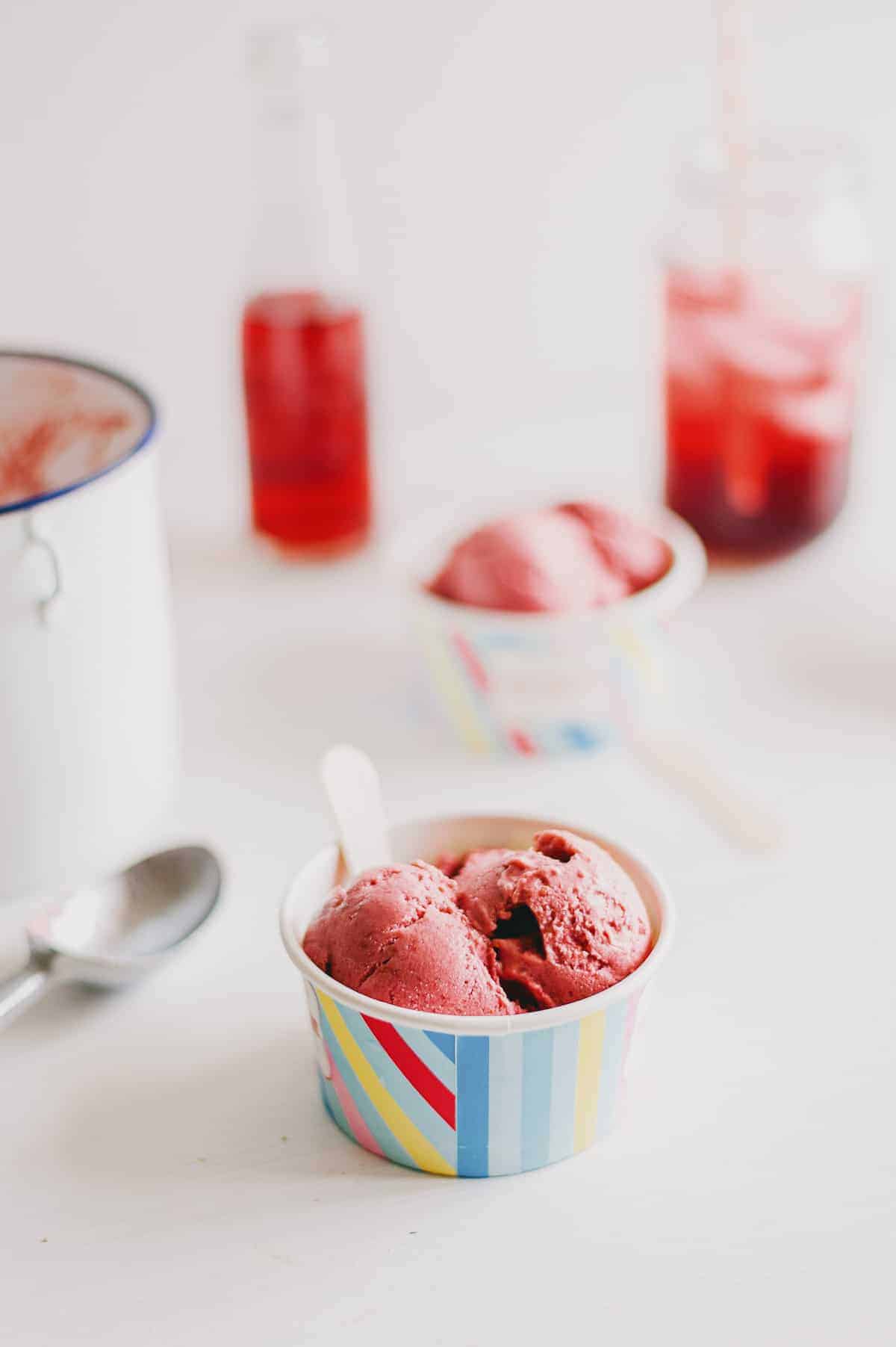 a white table with a small tub of ice cream with two red drinks in the background