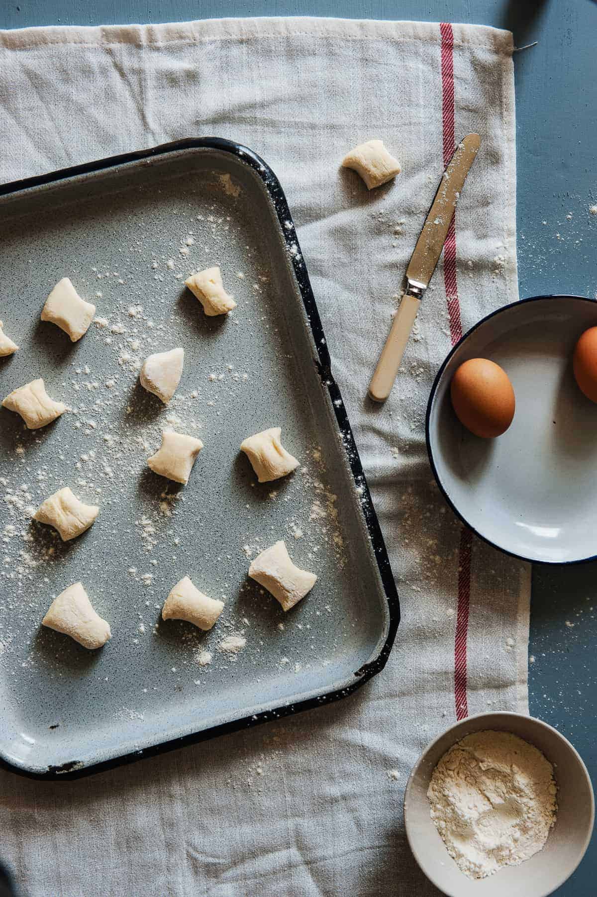 top down view of ricotta gnocchi on a tray with eggs and flour next to them