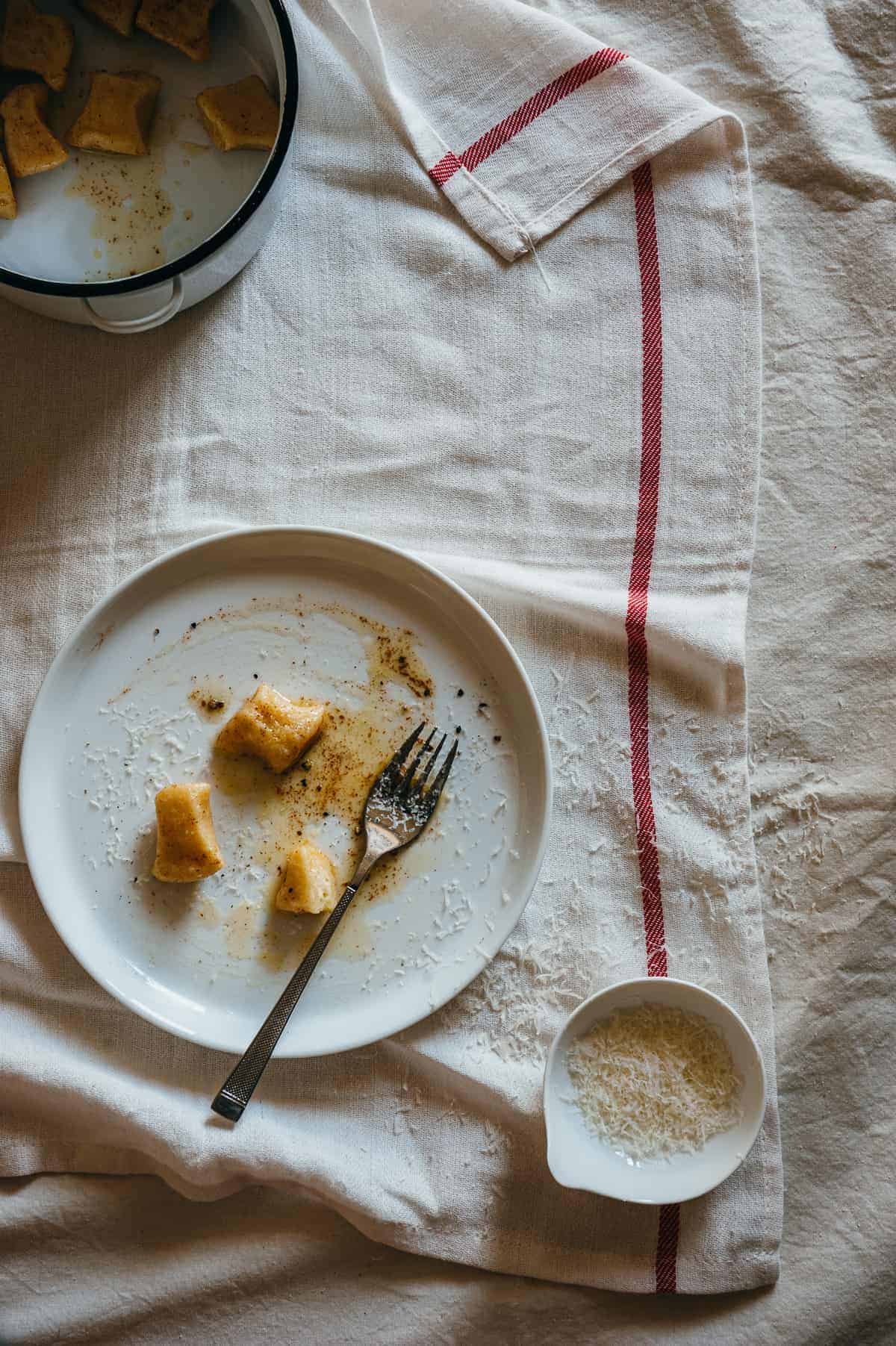 top down view of ricotta gnocchi served on a white plate with a small bowl of grated cheese