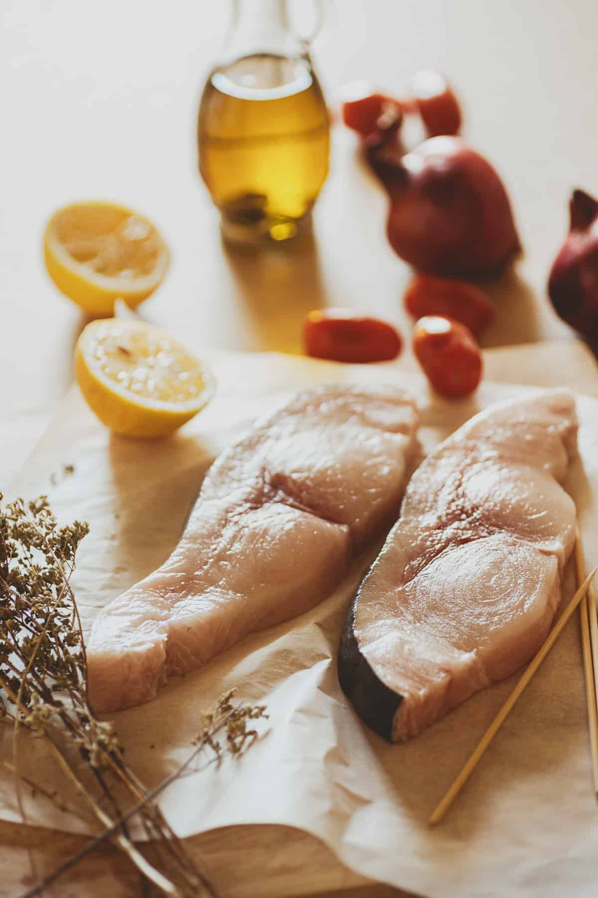 two swordfish steaks with herbs, lemon, onions, tomatoes and olive oil on a table