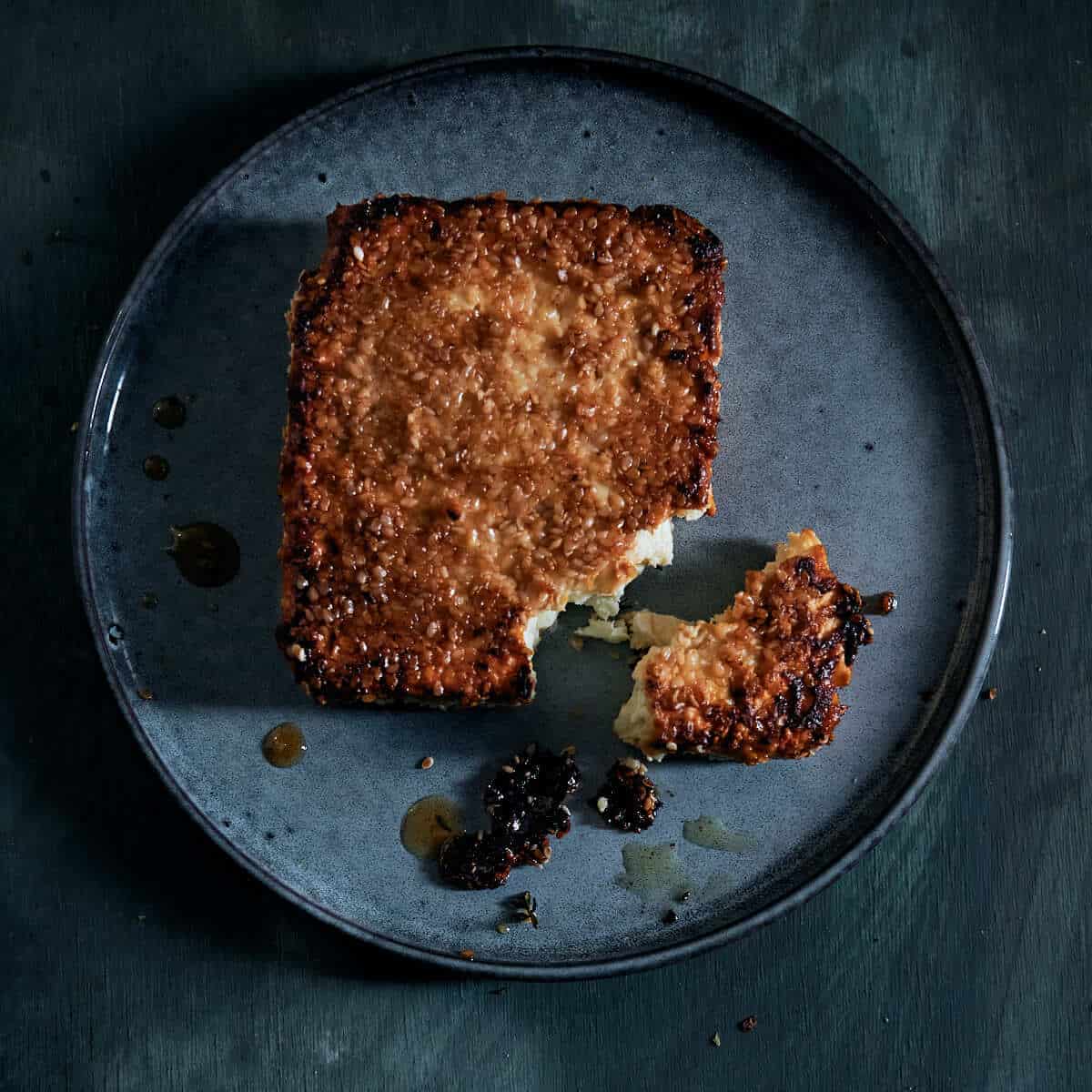 a block of cooked cheese on a plate encrusted with sesame seeds