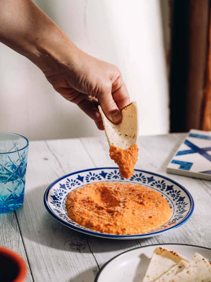 a hand dipping pita bread into a plate with dip