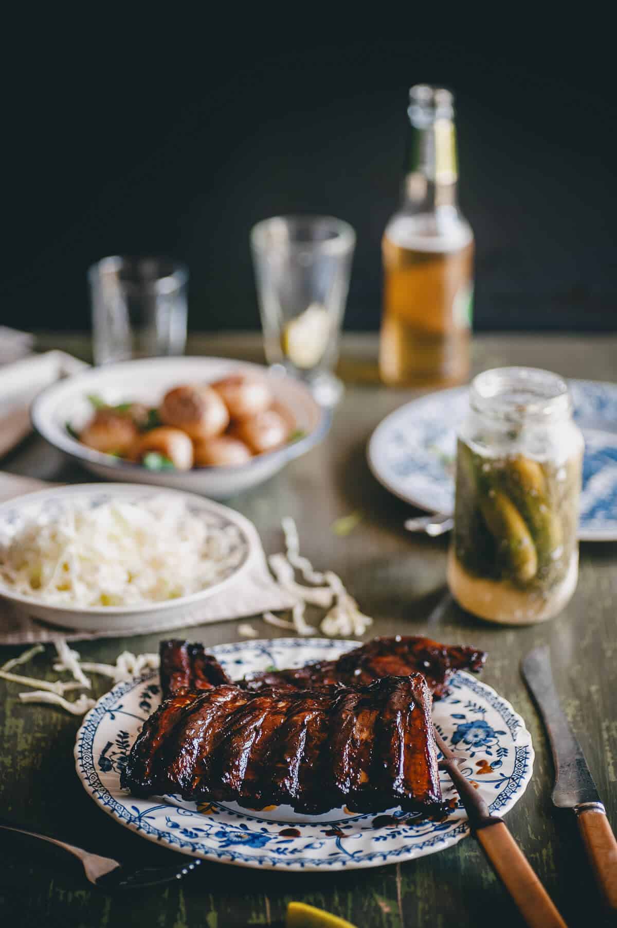 cooked ribs on a plate with coleslaw, baked potatoes and pickles