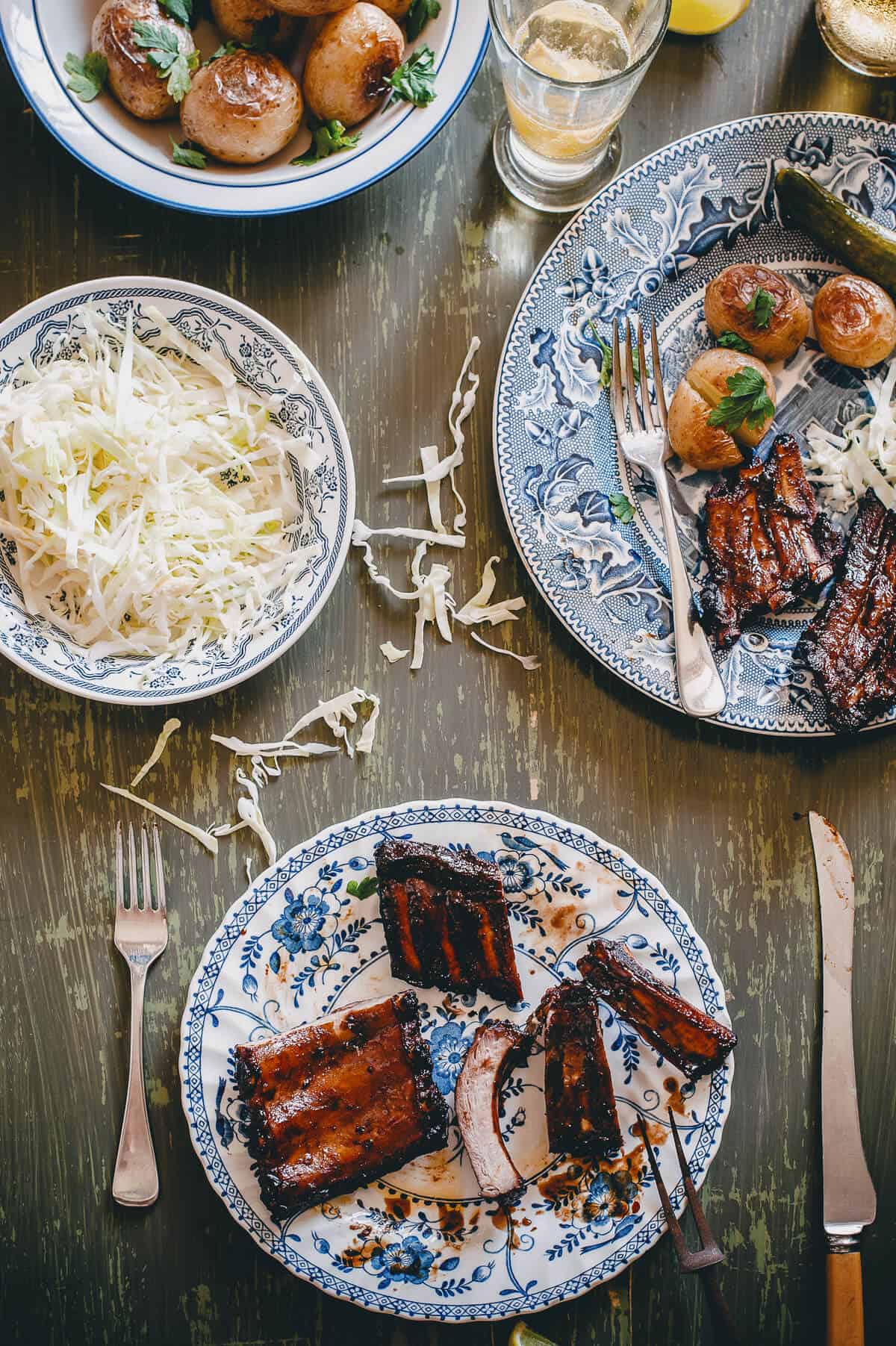 a table with cooked ribs coleslaw and baked potatoes