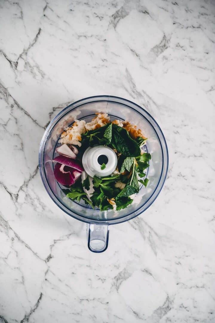 a food processor filled with mint, parsley soaked bread and onions