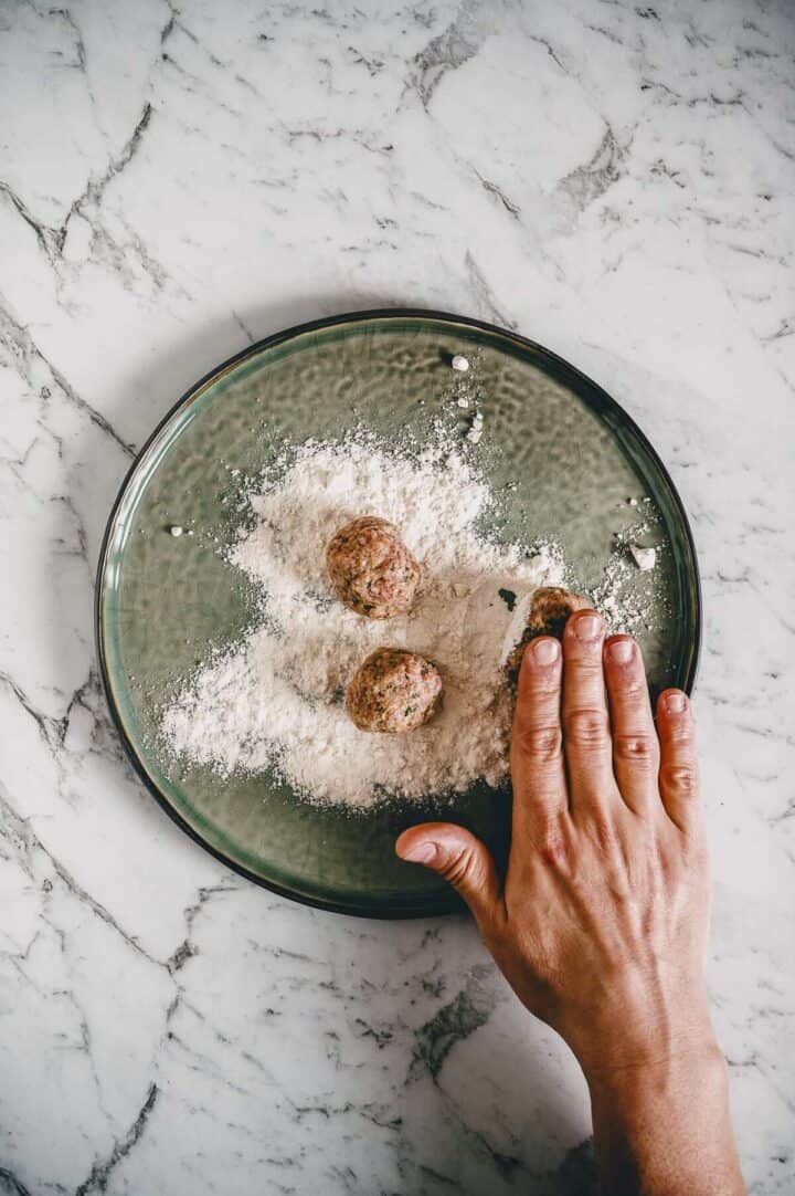 a hand dredging meatballs in flour